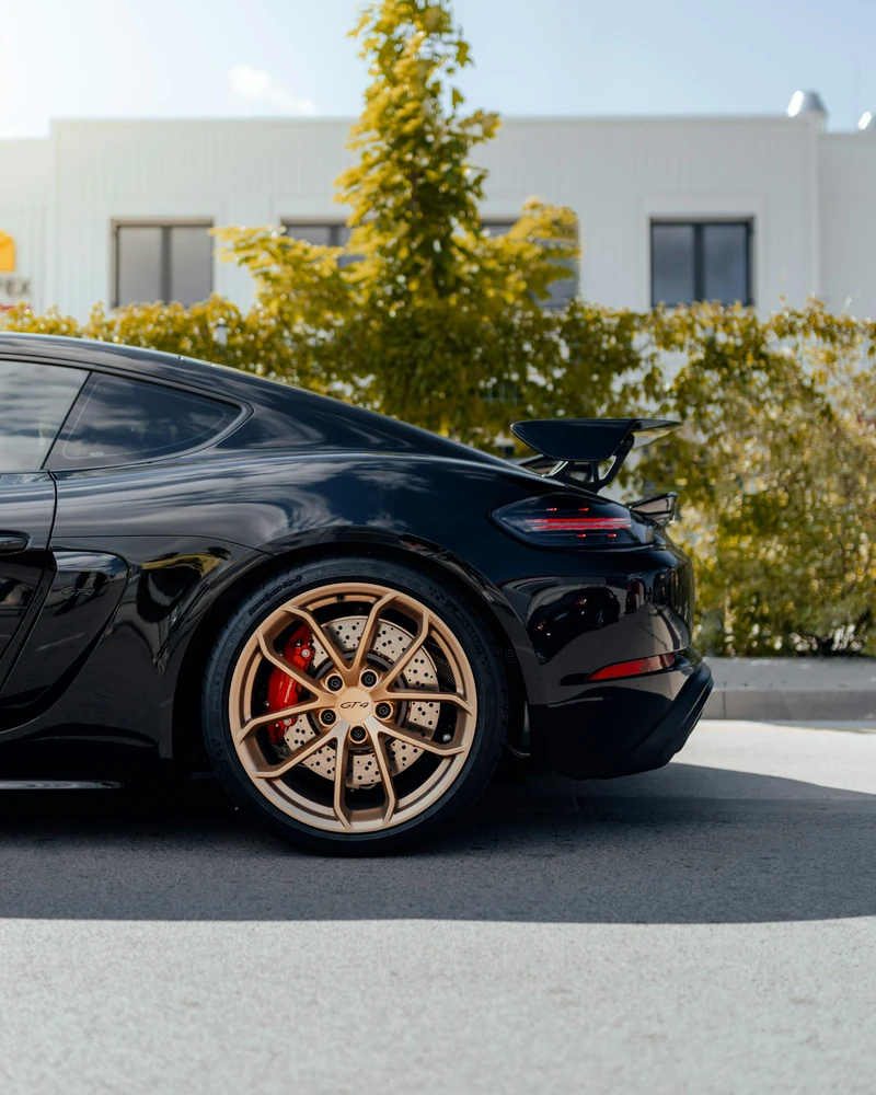 Rear quarter of a black Porsche Cayman GT4 with a gold wheel